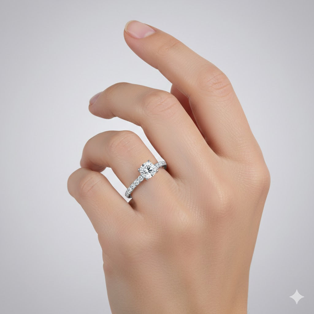 A hand with neatly manicured nails displays the Round-Cut Solitaire Lab Diamond Engagement Ring—a silver band with a round, sparkling lab diamond—set against a plain light gray background, perfect for an elegant engagement.