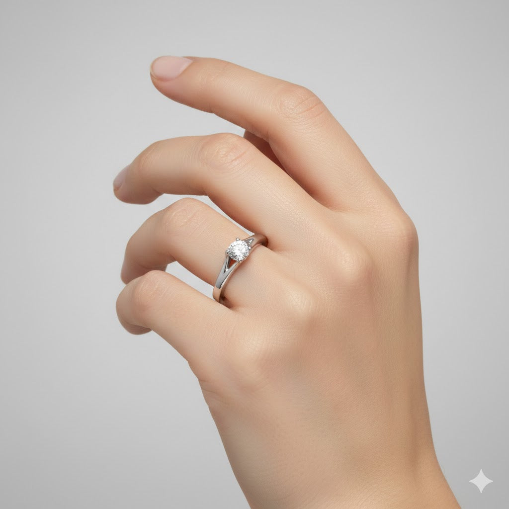 A hand with neatly manicured nails is shown against a plain background, wearing the Elegant Tapered Band Lab Diamond Engagement Ring featuring a single round stone on the ring finger.