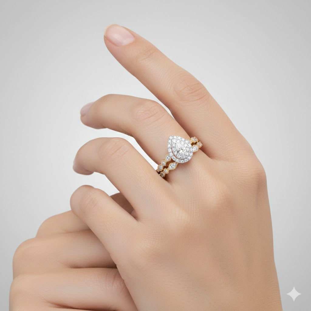 A hand with manicured nails displays the 10k Gold Pear Diamond Halo Bridal Ring Set 3/8 Cttw—an elegant engagement and wedding band duo—against a light gray background.