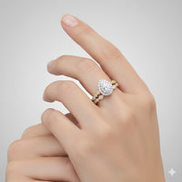A hand with manicured nails displays the 10k Gold Pear Diamond Halo Bridal Ring Set 3/8 Cttw—an elegant engagement and wedding band duo—against a light gray background.