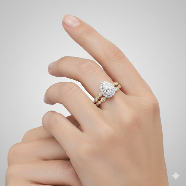 A hand with manicured nails displays the 10k Gold Pear Diamond Halo Bridal Ring Set 3/8 Cttw—an elegant engagement and wedding band duo—against a light gray background.