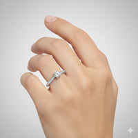 A hand with a light skin tone wears the Six-Prong Round Lab Diamond Solitaire Engagement Ring with Pave Accents, featuring a silver setting, pavé band details, and a round center diamond, displayed against a plain light gray background.