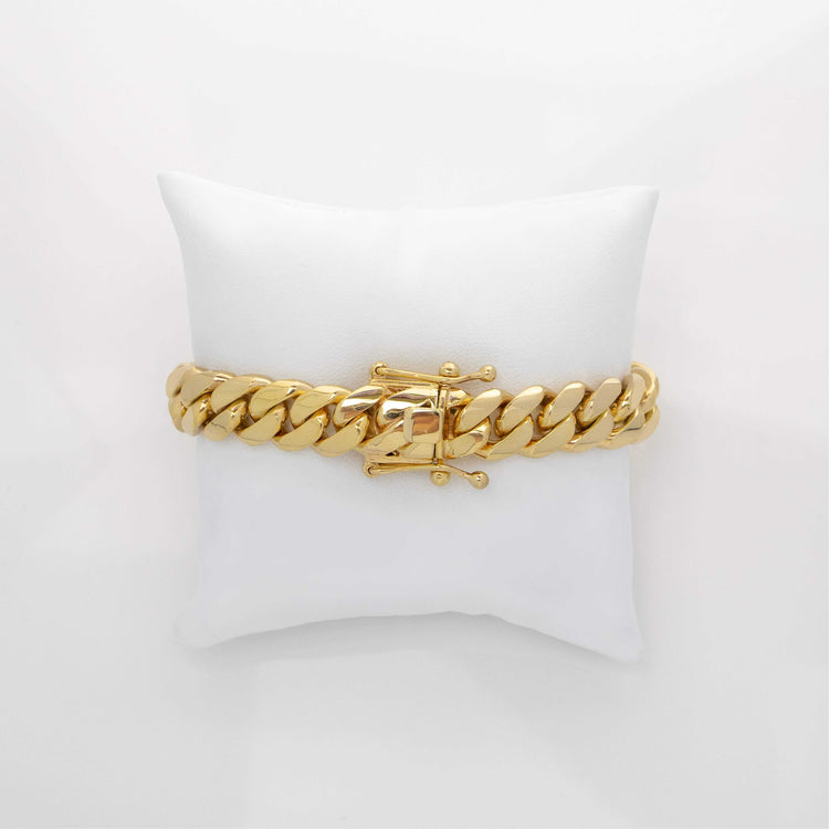 The 12mm Handmade Miami Cuban Link Bracelet in 10K, 14K, or 18K solid gold with a box clasp is elegantly displayed on a white cushioned pillow against a plain white background.