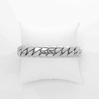 A thick, polished 15mm Cuban Link Bracelet - 15mm Solid Gold is displayed on a white cushioned pillow against a plain white background.