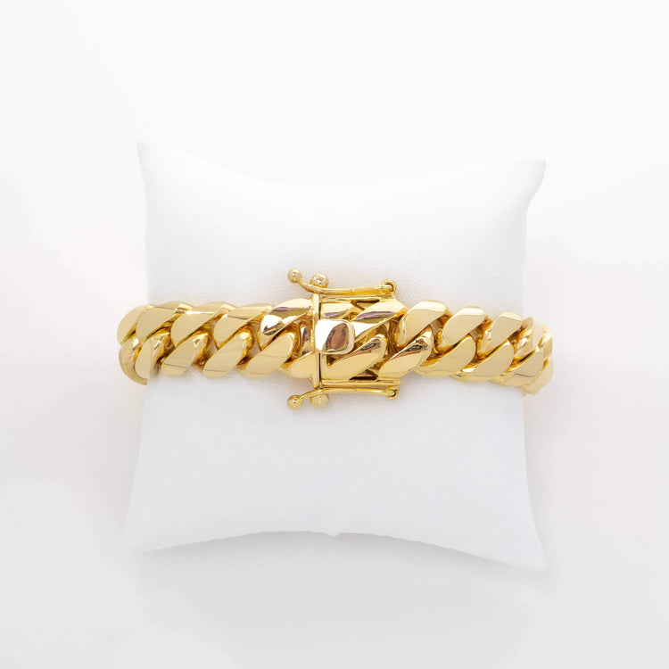 The 15mm Handmade Miami Cuban Link Bracelet in 10K/14K solid gold features thick, polished links and a box clasp closure, displayed on a white cushion to showcase its luxurious and elegant handmade design.