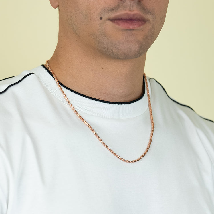 A man wears a white t-shirt with black trim and a 3mm Barrel Crystal Chain - 14k Rose Gold Bonded necklace, shown from shoulders to chin against a light background.