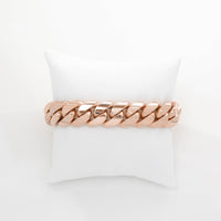 The Cuban Link Bracelet - 16mm Solid Gold is displayed on a white cushioned stand against a plain white background.