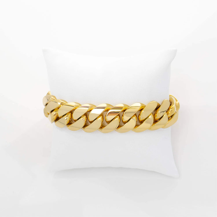The 18mm Handmade Miami Cuban Link Bracelet in 10K/14K solid gold, featuring bold, flat links, is showcased on a white cushioned pillow against a plain white background—an elegant display of timeless luxury.