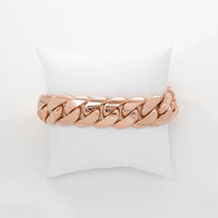 The Cuban Link Bracelet - 19mm Solid Gold is showcased on a white cushioned pillow, with a plain white background highlighting its bold design.