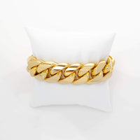 The Cuban Link Bracelet - 20mm Solid Gold features large, interlocking links and is elegantly displayed on a white cushioned stand against a plain white background.