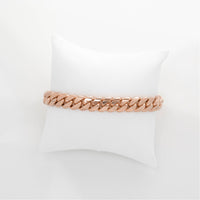 The Cuban Link Bracelet - 9mm Solid Gold in rose gold is shown on a white cushioned pillow, set against a plain white background.