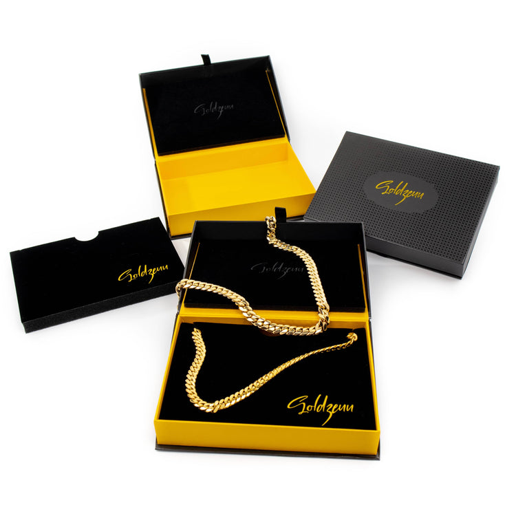 A Cuban Link Chain 10mm - 14k Gold Bonded is showcased in an open yellow and black Goldzum box, with matching men's jewelry packaging displayed around it.