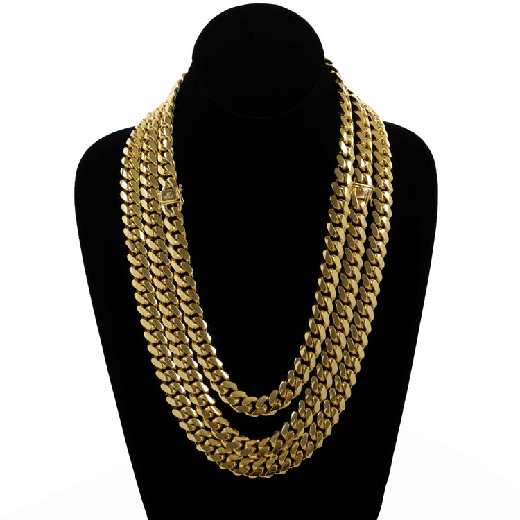 The Cuban Link Chain 12mm - 14k Gold Bonded is displayed on a black velvet bust with thick, layered gold chains featuring flat, interlocking links. Expertly crafted for lasting shine, against a plain white background.