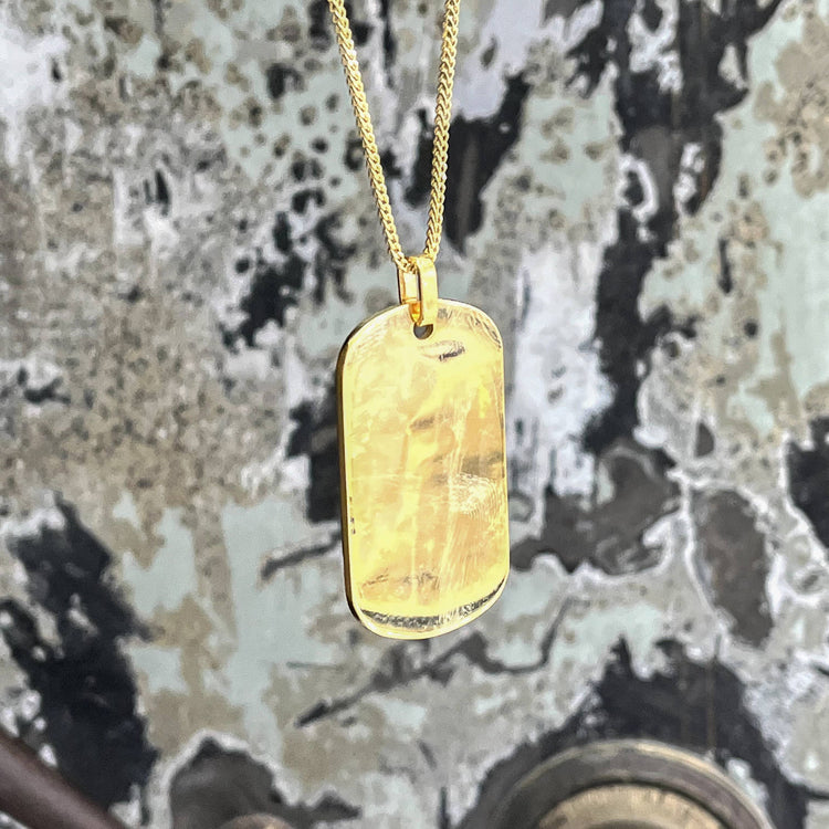 The Custom Military/Dog Tag Pendant with a rectangular charm hangs against a weathered wall with peeling black, tan, and gray paint.