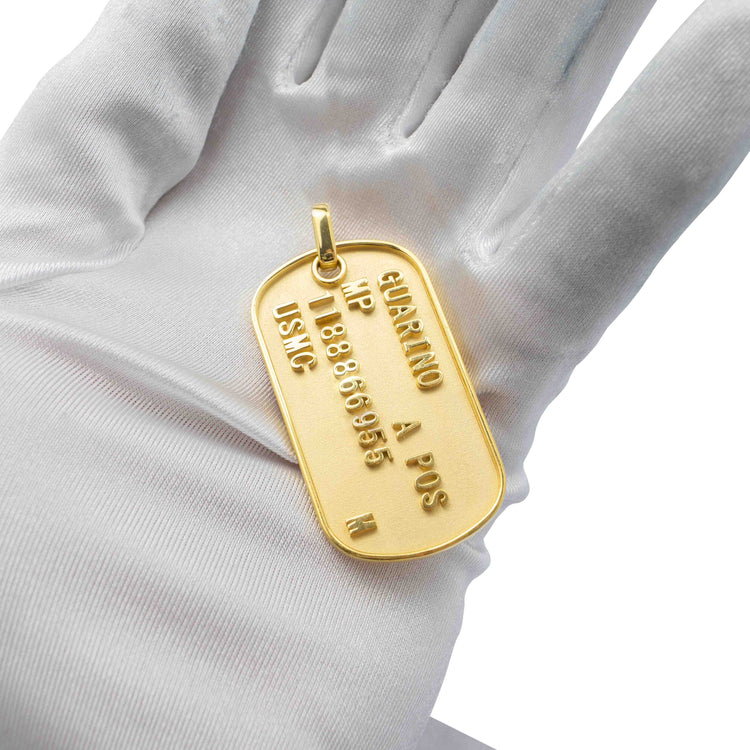 A gloved hand holds a Custom Military/Dog Tag Pendant, engraved with a name, blood type, and identification number.