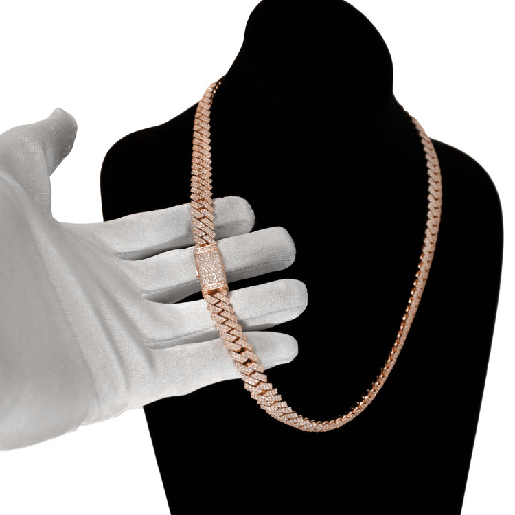 A hand in a white glove holds the Diamond Cuban Link Chain – 8mm-17.5mm Solid Rose Gold, featuring a diamond-encrusted clasp, elegantly displayed on a black velvet bust against a white background.