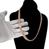 A hand in a white glove holds the Diamond Cuban Link Chain – 8mm-17.5mm Solid Rose Gold, featuring a diamond-encrusted clasp, elegantly displayed on a black velvet bust against a white background.