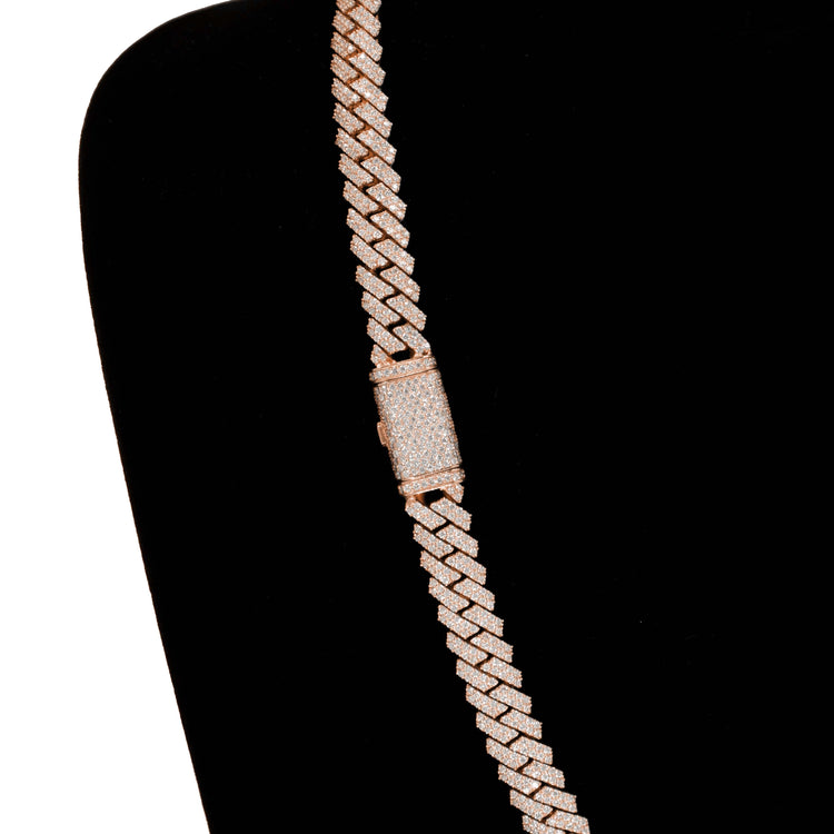 The Diamond Cuban Link Chain – 8mm-17.5mm Solid Rose Gold glistens with diamonds and features a bold rectangular diamond-studded clasp, displayed diagonally on black velvet for a stunning presentation.