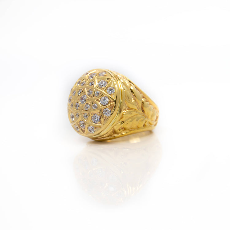 The Round Cluster Ring in Solid Gold features intricate engraved details and a rounded top adorned with sparkling round-cut stones in a geometric pattern, shown on a white background.