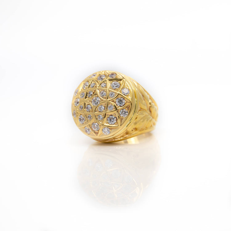 The Round Cluster Ring in Solid Gold features a large, round dome top adorned with sparkling stones in a geometric pattern, beautifully displayed on a white reflective surface.