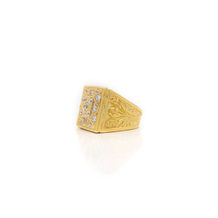 The Square Cluster Ring in Solid Gold showcases an engraved leaf pattern on the band and a rectangular face set with clear gemstones, presented against a white background with a subtle reflection.