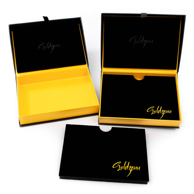 Three rectangular black and yellow boxes, two open to show yellow interiors and one closed. “Soldzenu” appears in gold on the packaging—ideal for the Tricolor Milano Figarope Chain, a 3.5mm 14K solid gold piece.