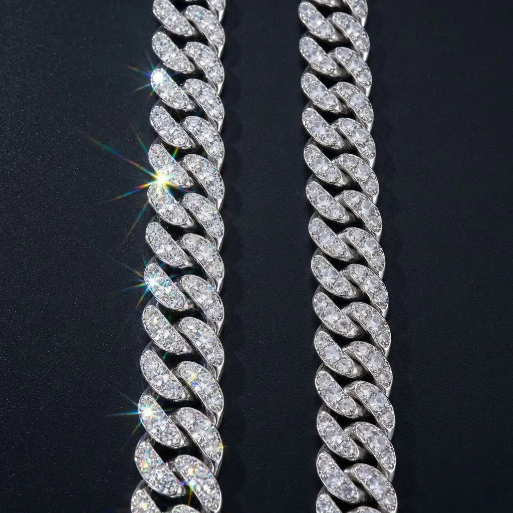 Side-by-side comparison of moissanite Cuban link chain with brilliant clear stones showing intense fire versus a CZ chain with slightly duller, less refractive stones on dark surface
