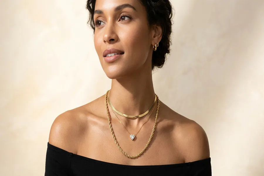 Elegant woman wearing layered solid gold necklaces including a choker, pendant, and long chain against a clean background — GOLDZENN women's necklace collection