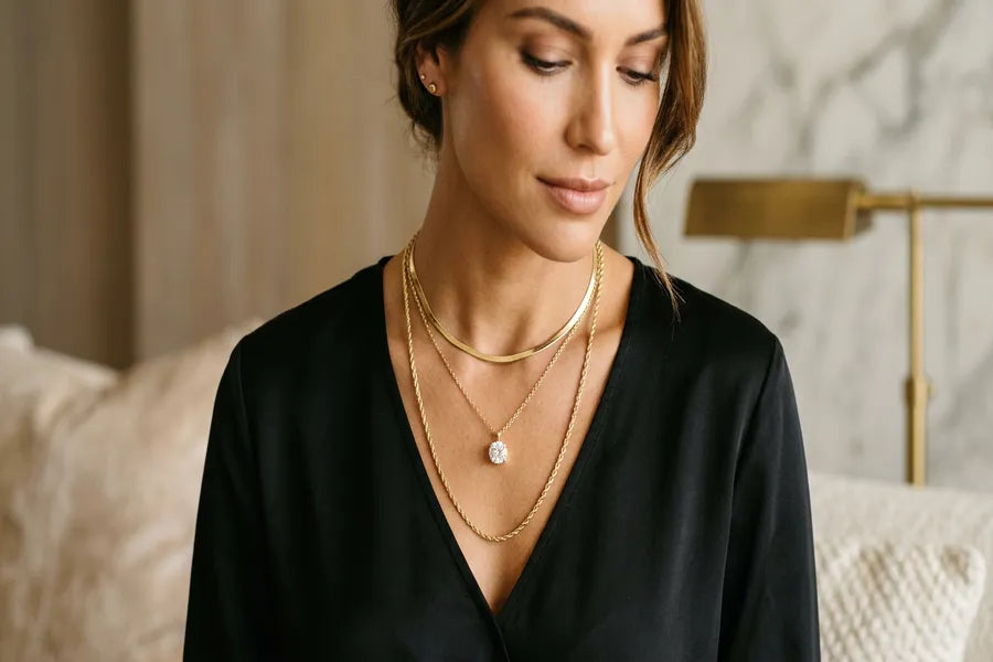 Woman demonstrating three-necklace layering technique with gold choker, pendant necklace, and long chain against a simple black top — GOLDZENN layering guide