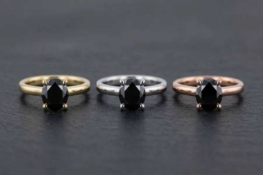 Tres anillos solitarios de diamantes negros idénticos comparando la diferencia visual entre engastes de oro amarillo de 10K, oro blanco de 14K y oro rosa de 18K
