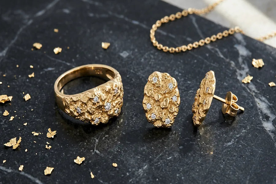 GOLDZENN gold nugget ring and diamond nugget earrings arranged on dark marble surface with warm lighting